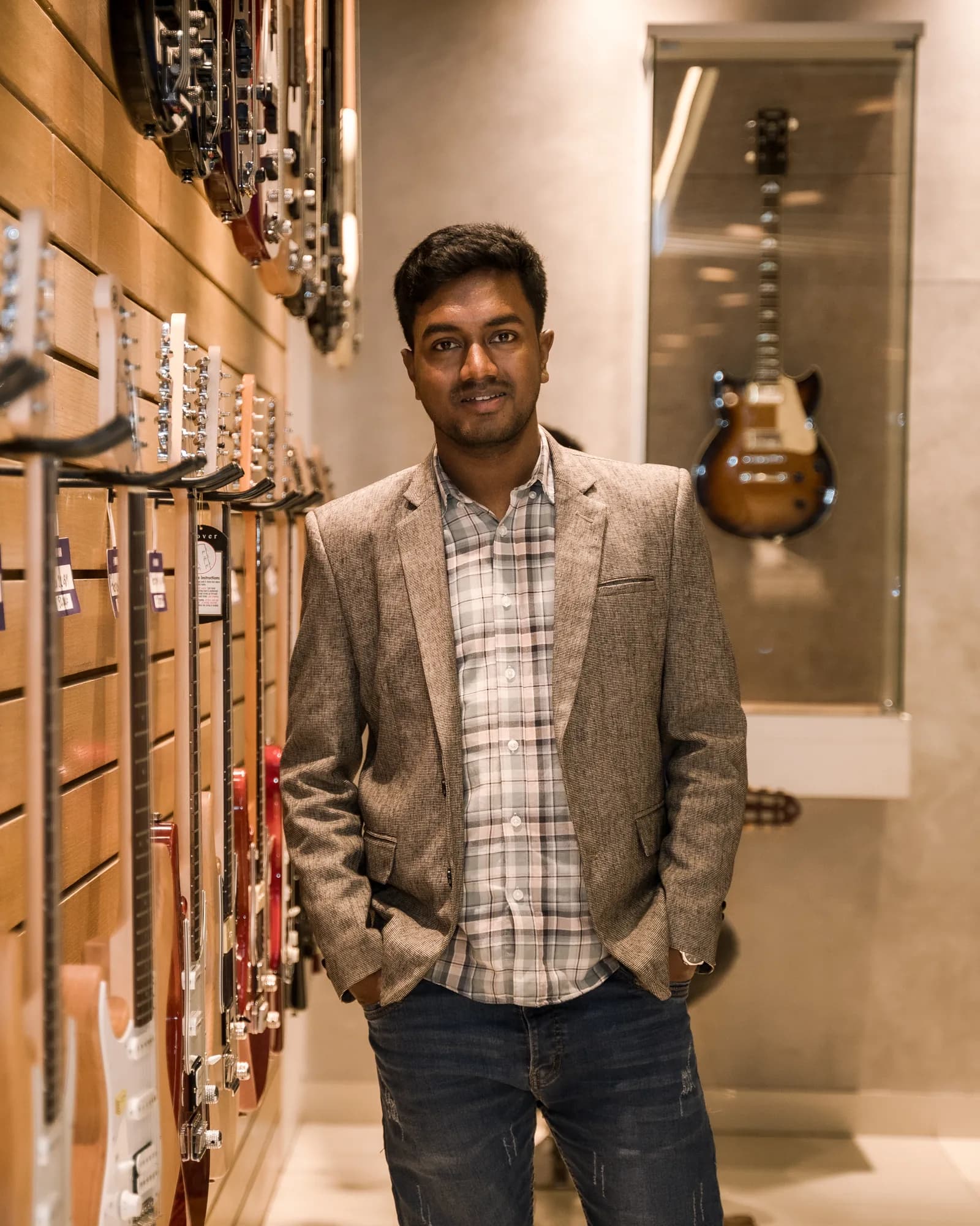 Razu Rahman standing beside a wall of guitars in a music showroom